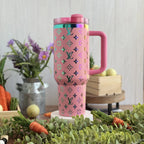 A pink thermos mug with a pink handle and a pink lid, placed on a wooden surface surrounded by various objects such as flowers, carrots, and a wooden crate.